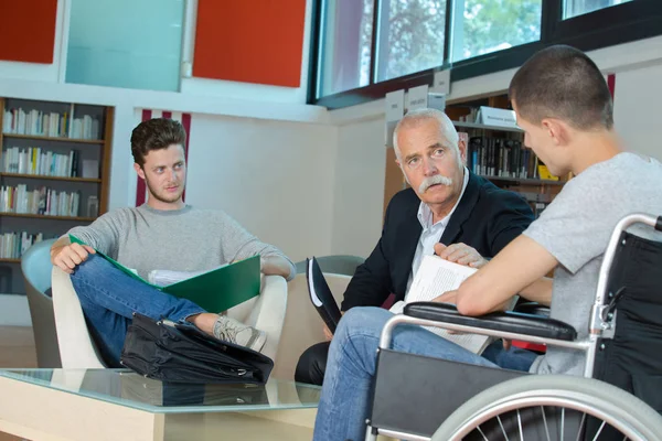 Студент в инвалидной коляске за стойкой в библиотеке колледжа — стоковое фото