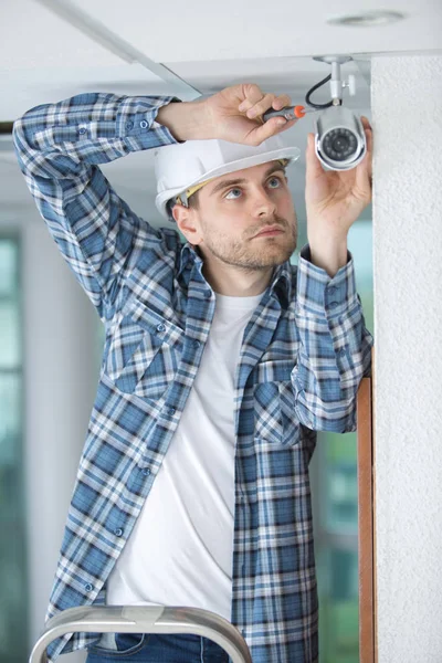 Молодой техник настраивает камеру на стене — стоковое фото