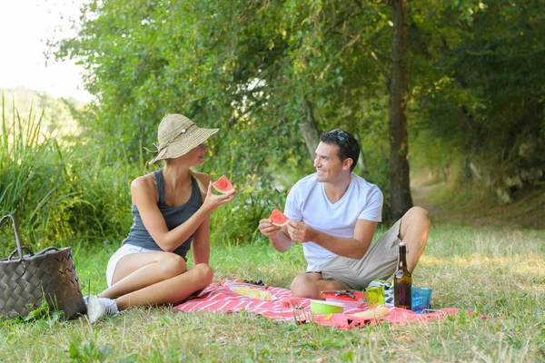 Coppia seduta su una coperta da picnic e mangiare anguria — Foto Stock