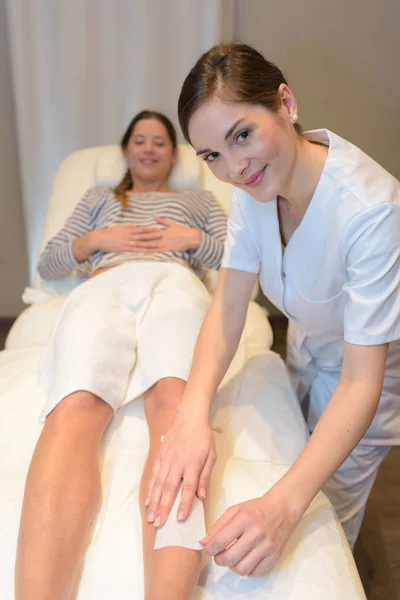 Kosmetyczka robi depilacji do nogi kobieta z taśmy woskowe — Zdjęcie stockowe
