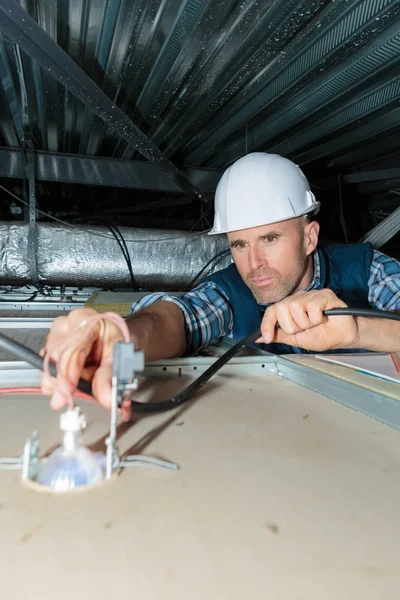 Mann auf der Leiter legt Licht an die Decke — Stockfoto