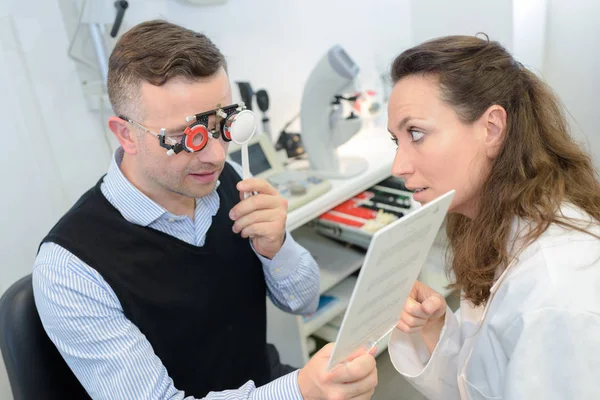 Женщина-оптик в хирургии проводит тест на зрение для мужчин — стоковое фото