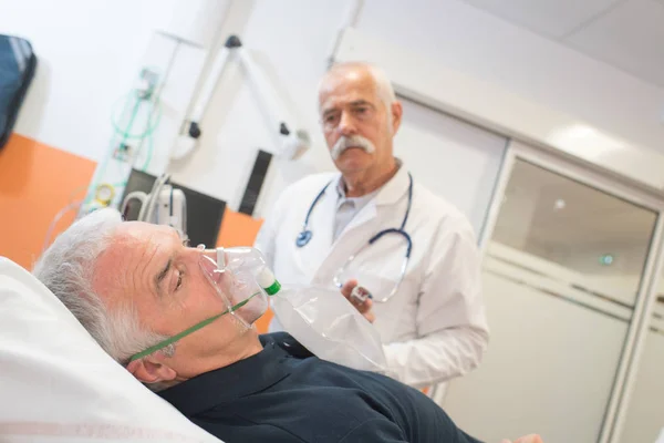 Lékař při pohledu na starší mužský pacienta vdechují přes kyslíkovou masku — Stock fotografie