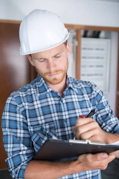 Junge Architektin im Helmaufbau stehend und schreibend auf Klemmbrett — Stockfoto