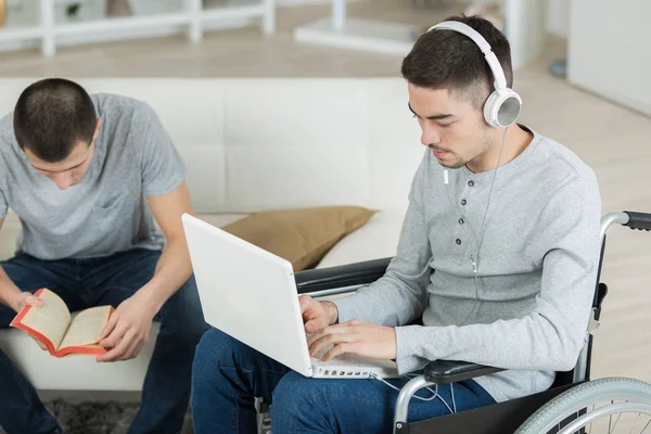 Uomo lettura libro, amico disabile utilizzando il computer portatile — Foto Stock