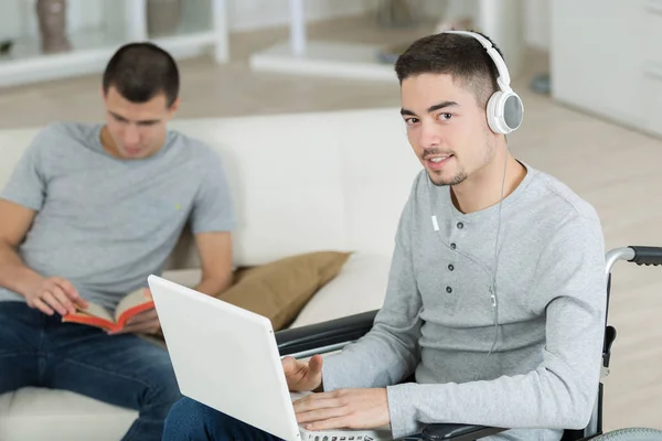 Behinderter Jugendlicher schaut auf Laptop und trägt Kopfhörer — Stockfoto