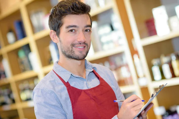 Man holding bottle of wine and writing on clipboard — Stock Photo, Image