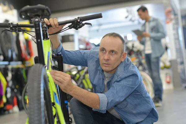 Hombre comprueba bicicleta antes de comprar en la tienda de deportes —  Fotos de Stock