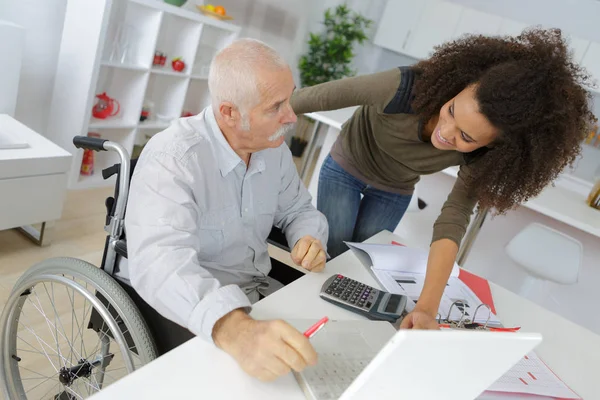 Jonge dame helpen rolstoel man computer te gebruiken — Stockfoto