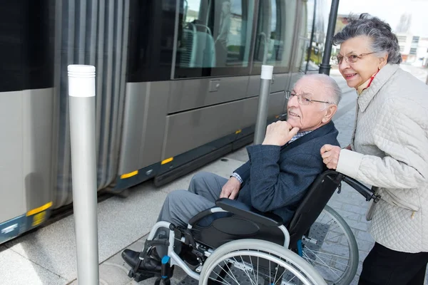 Idosa empurrando cadeira de rodas marido amarrado em bonde — Fotografia de Stock