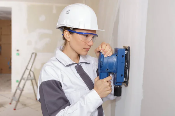 Vrouwelijke Stukadoor schuren van de muur met behulp van een power-schuurmachine — Stockfoto