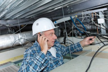 builder checkking ceilings cables while using the phone clipart