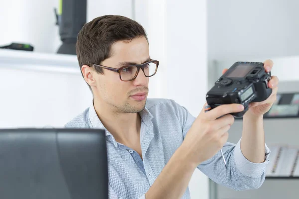 Giovane tecnico fiducioso sta fissando e pulendo una fotocamera digitale — Foto Stock