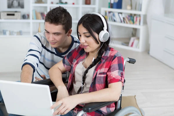 Junge Leute schauen auf Laptop, Mädchen im Rollstuhl — Stockfoto