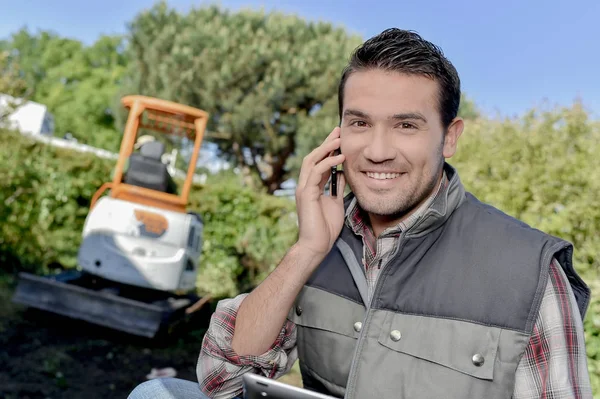 Man outdoors on telephone, digger in background — Stock Photo, Image