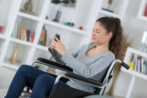 Jovem mulher em uma cadeira de rodas usando telefone celular — Fotografia de Stock