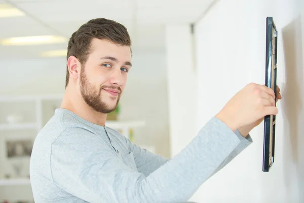 Homem colocando quadro de imagem na parede — Fotografia de Stock