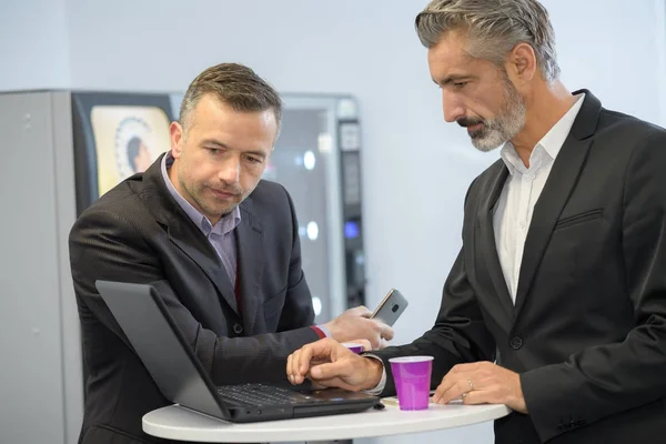 Uomini da distributori automatici guardando il computer portatile — Foto Stock