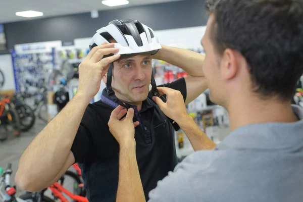 Hombre sonriente en casco selecciona bicicleta en tienda de artículos deportivos — Foto de Stock