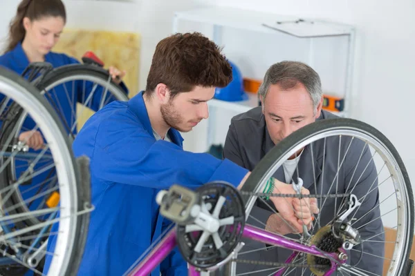 Mecânico de bicicletas e aprendizes reparando uma bicicleta na oficina — Fotografia de Stock