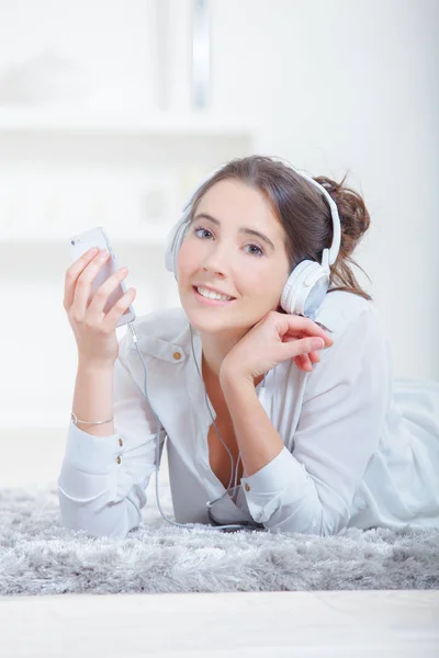 Lady liggend op tapijt, luisteren naar de hoofdtelefoon — Stockfoto