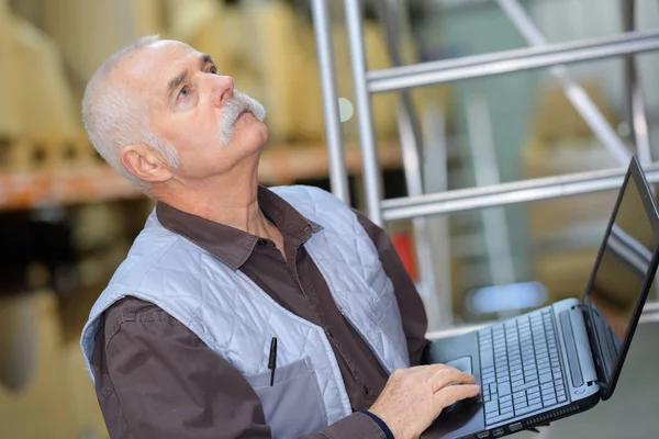 Focused warehouse manager working on laptop in a large warehouse — Stock Photo, Image