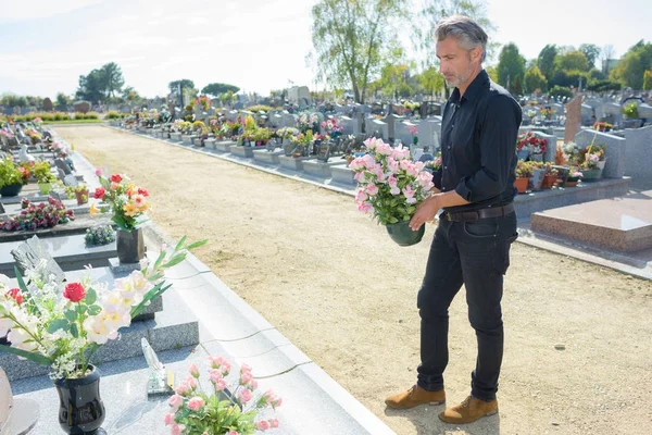 Homem segurando flores para colocar na sepultura — Fotografia de Stock