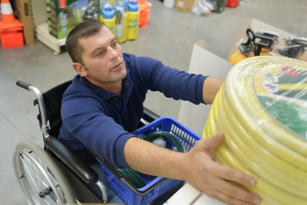 Disabled man struggling to reach a hose at gardening store — Stock Photo, Image