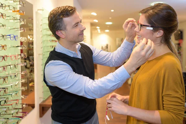 Офтальмолог и красивая брюнетка выбирает очки в магазине оптики — стоковое фото