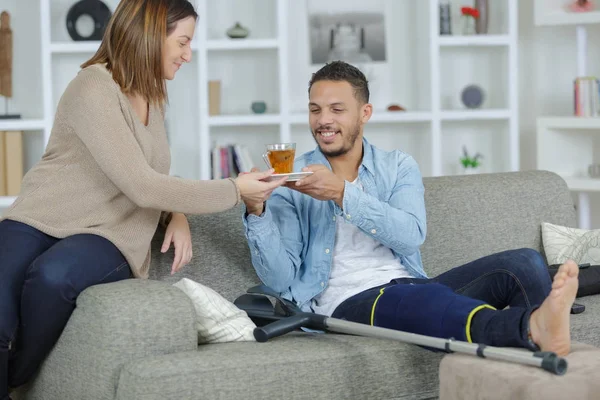 Lady passing a hot drink to injured man — Stock Photo, Image