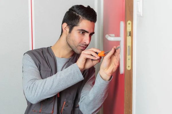 Jovem consertando a porta com chave de fenda — Fotografia de Stock