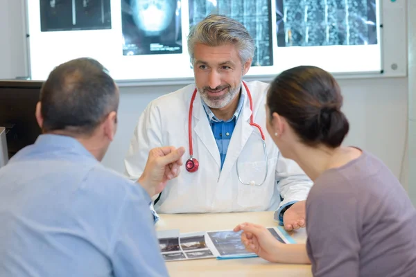Médico do sexo masculino mostrando resultados de raios-x para casal na clínica — Fotografia de Stock