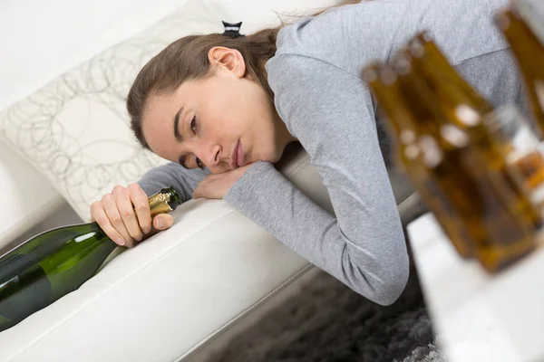 Alcoholic addict woman lying on the sofa hangovered with bottles — Stock Photo, Image