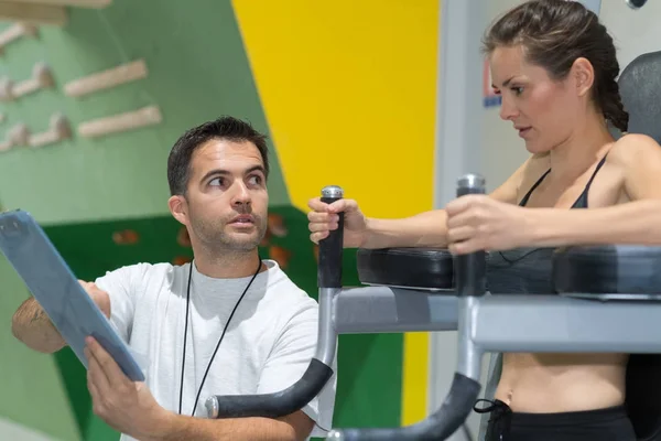 Женщина упражнения в тренажерном зале с некоторой помощью личного тренера — стоковое фото