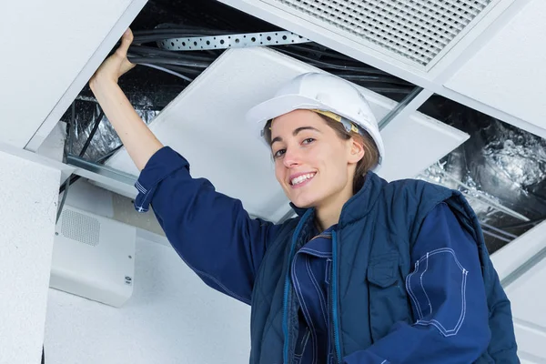 Vrouwelijke elektricien installeert elektrisch apparaat in plafond — Stockfoto