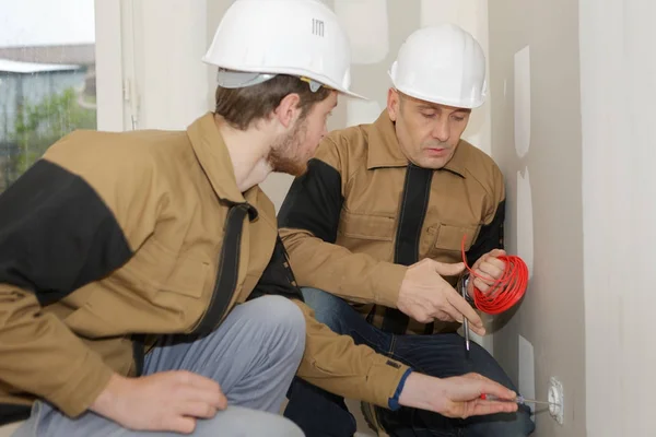 Aprendiz eletricista com supervisor segurando cabo por tomada plug — Fotografia de Stock