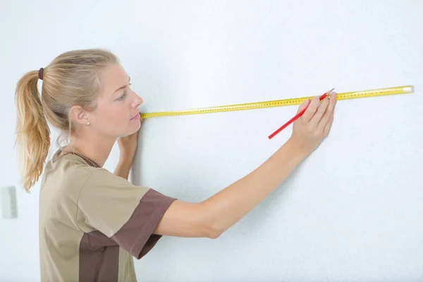 Femme mesurant un mur avec niveau d'esprit dans la chambre — Photo