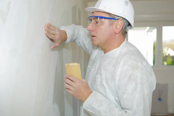 Construtor sênior lixar a parede com uma esponja de lixar — Fotografia de Stock