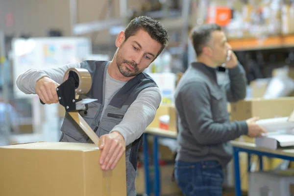 Man aan het werk bij magazijn terwijl de manager aan de telefoon — Stockfoto