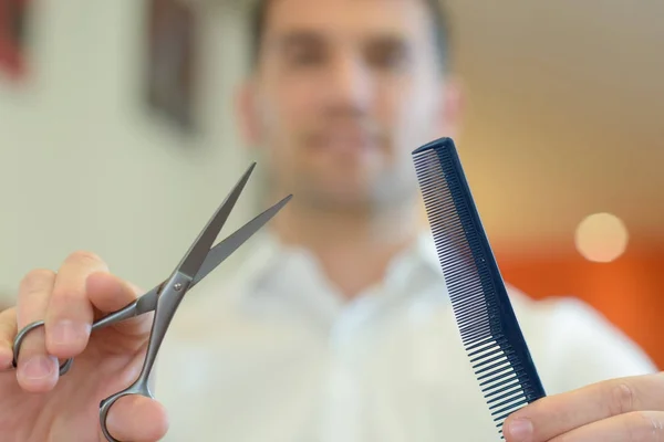 Barber holding scissors and comb into foreground