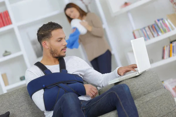Man with arm in sling using computer woman dusting — Stock Photo, Image