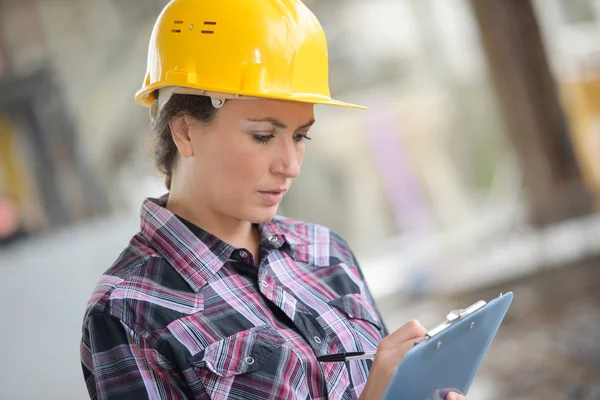 Signora che indossa hardhat scrittura sugli appunti — Foto Stock