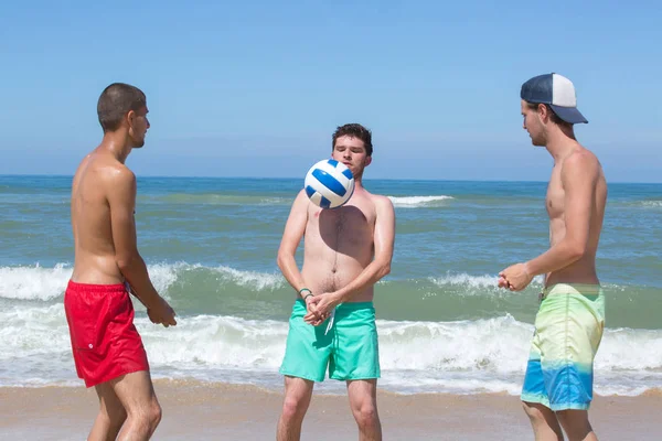 Grupp unga glada män spelar volleyboll på stranden — Stockfoto