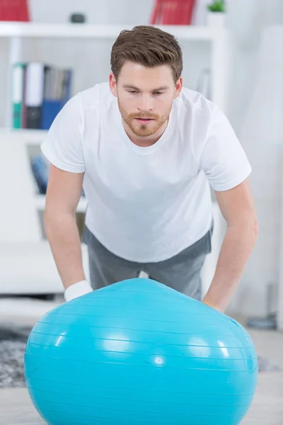 Atractivo joven con pelota suiza haciendo ejercicios en casa — Foto de Stock