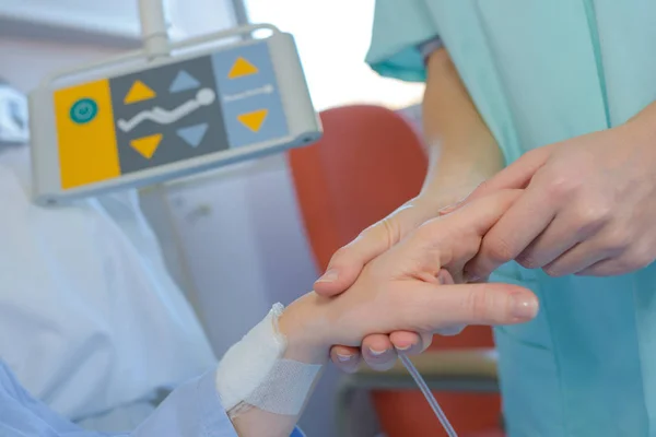 Krankenschwester hält geduldige Hand auf einem Bett — Stockfoto
