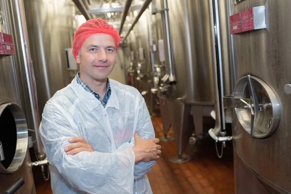 Homem alegre em uniforme branco posando perto de tanques na cervejaria — Fotografia de Stock