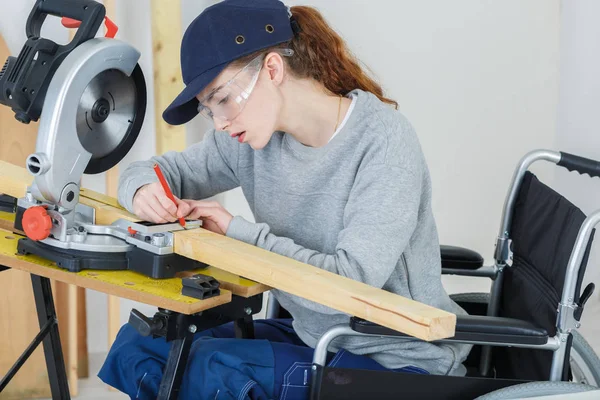 Kvinnliga snickare på rullstolen med hjälp av en cirkelsåg — Stockfoto