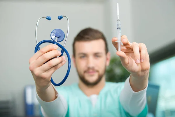 Jovem médico segurando seringa e estetoscópio — Fotografia de Stock