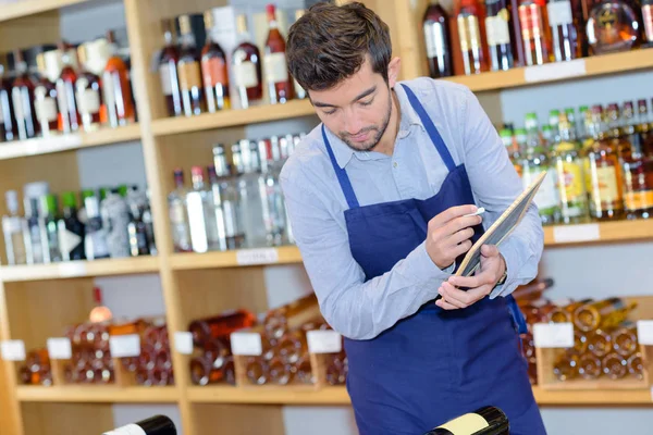 Lachende verkoper man draagt schort in wijnwinkel — Stockfoto