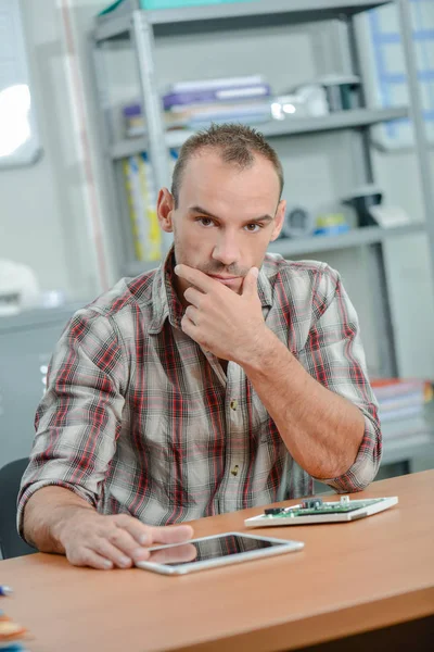 Man sitter vid skrivbord med tablett Stockbild